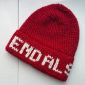 A red crochet hat is lying on a white background. White letters on the hat brim spell out "End ALS"