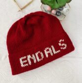 A red knit hat is lying on white background. White letters on the hat brim spell "End ALS"