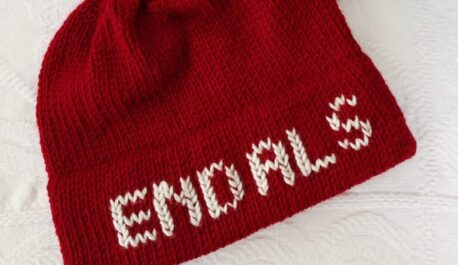 A red knit hat is lying on white background. White letters on the hat brim spell "End ALS"