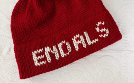 A red knit hat is lying on white background. White letters on the hat brim spell "End ALS"