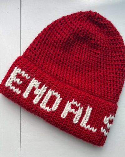 A red crochet hat is lying on a white background. White letters on the hat brim spell out "End ALS"